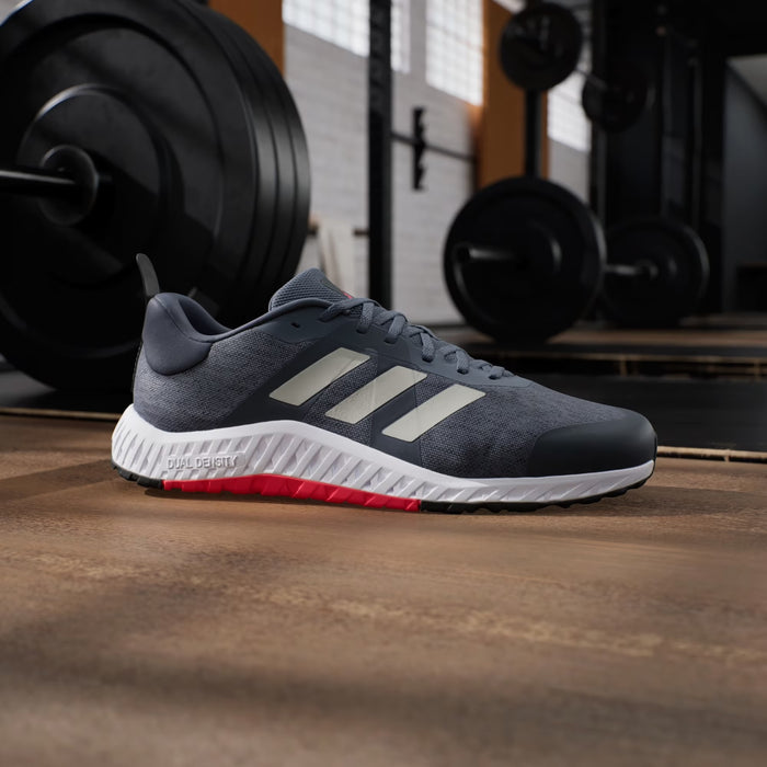 Adidas Everyset Trainer shoes in dark gray with white and red accents, featuring a Dual Density midsole, side view in gym setting.