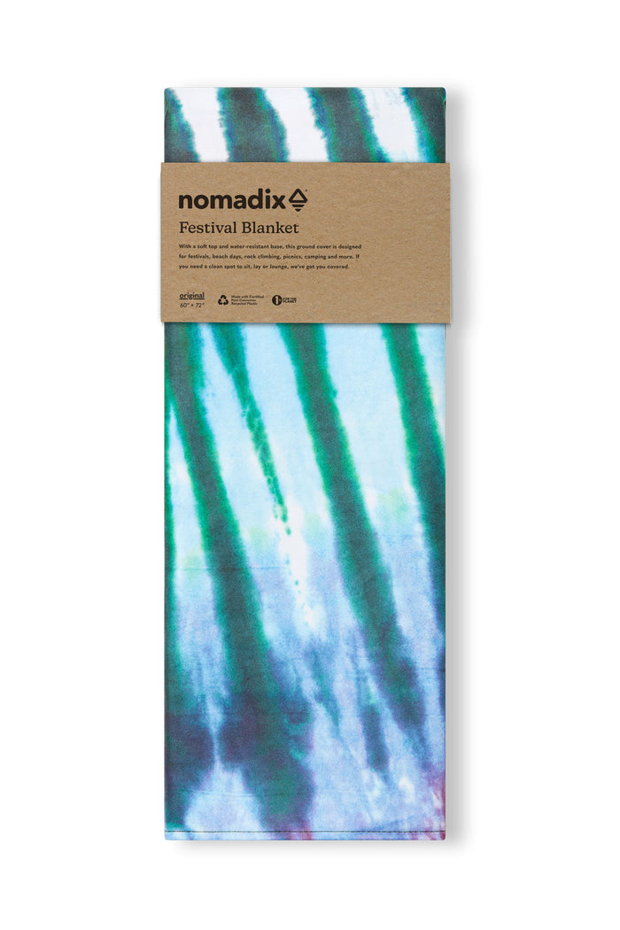 Nomadix Festival Blanket in tie-dye pattern with blue, green, and purple hues, compactly folded and packaged, front view.