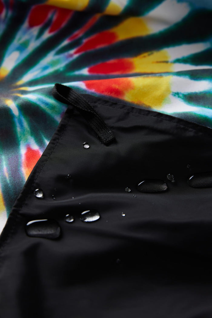 Nomadix Festival Blanket with black water-resistant corner and colorful tie-dye pattern, close-up view.