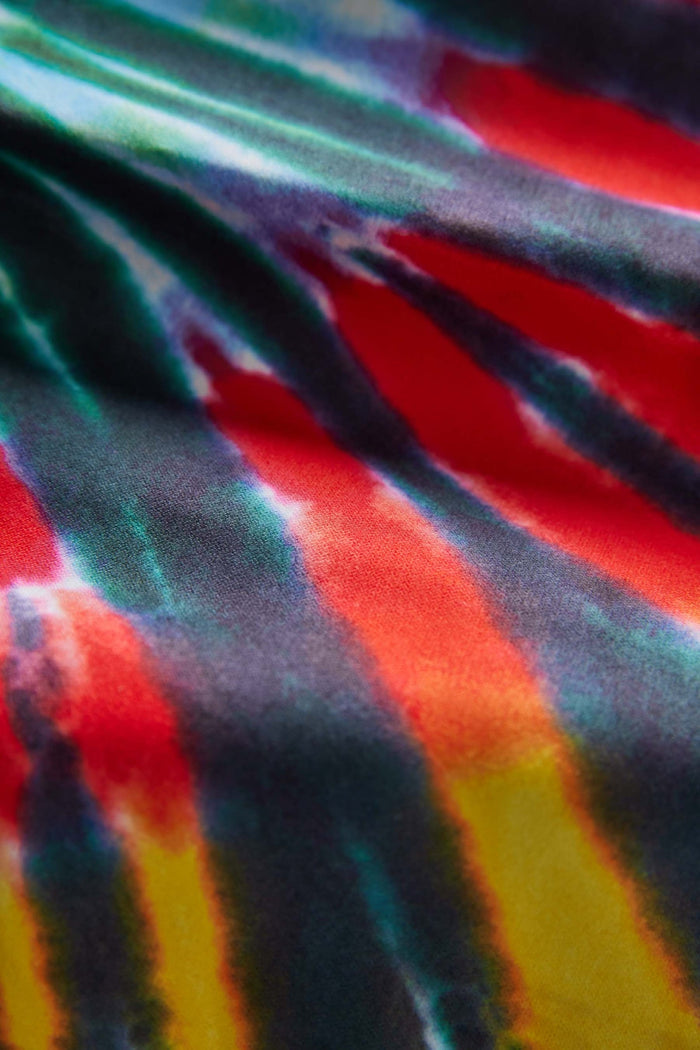 Nomadix Festival Blanket featuring a vibrant tie-dye design with red, yellow, green, and blue hues, close-up view of fabric texture.