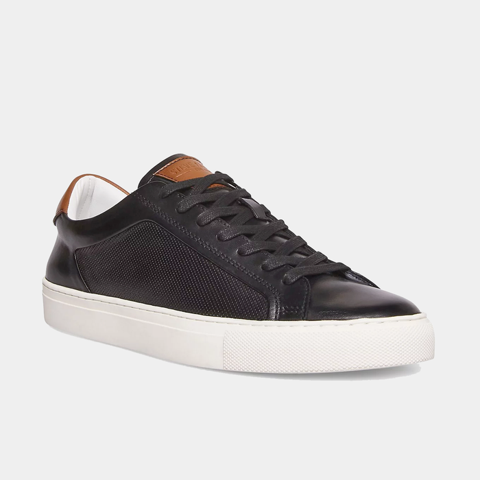 Steve Madden Finneas sneakers in black leather and textured side panels with brown heel accents, white rubber sole, angled front view.