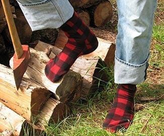 Polar Feet Fleece Socks in red and black plaid pattern, thick fleece material, worn outdoors near wood logs.