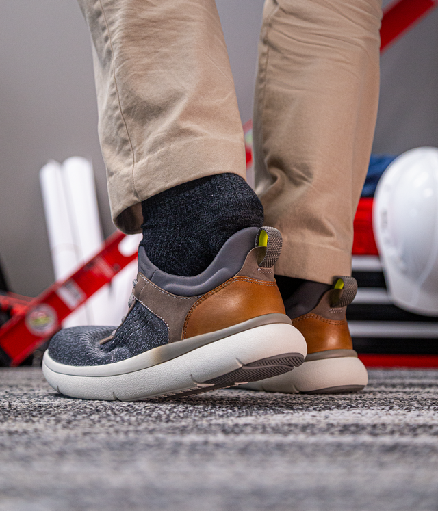 Florsheim Work Fleet Work Comp Toe Sneaker in gray knit and brown leather with cushioned outsole, worn by a worker indoors.