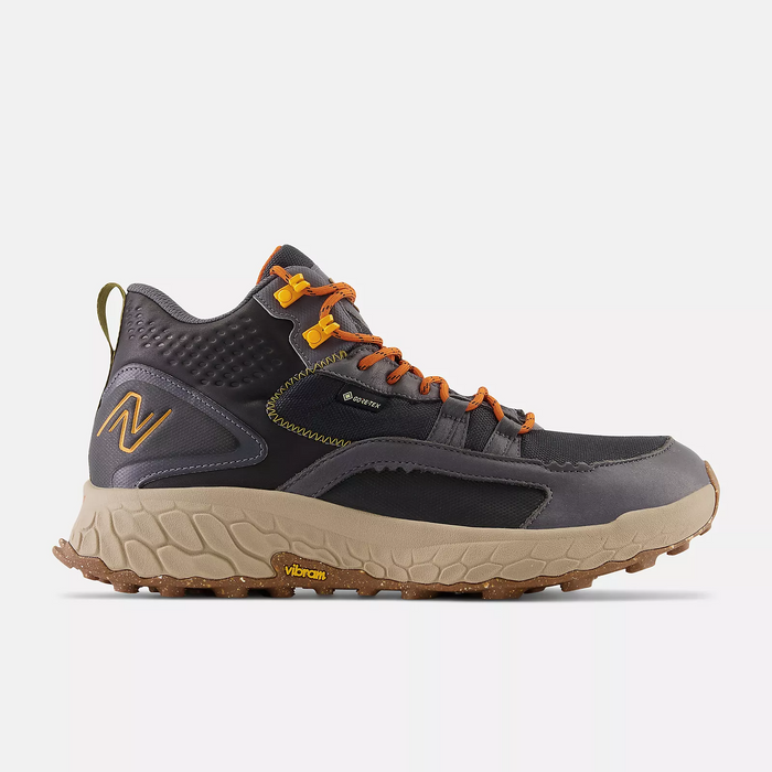 New Balance Foam X Hierro Mid GTX hiking boots in dark gray with orange accents, Gore-Tex upper, and beige Vibram outsole, side view.