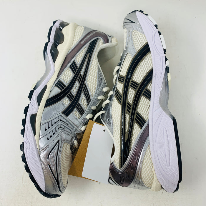 Brand new ASICS Gel-Kayano 14 Cream Black Metallic Plum sneakers rest elegantly on a pristine brown ASICS shoe box. With a mesh upper, metallic accents, and black details, these shoes stand out against a neutral backdrop.