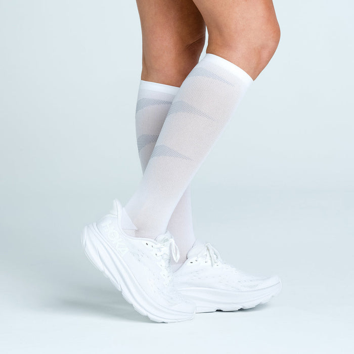 Feetures Graduated Compression Light Cushion socks in white with subtle gray pattern, knee-high design worn by a person with white sneakers.