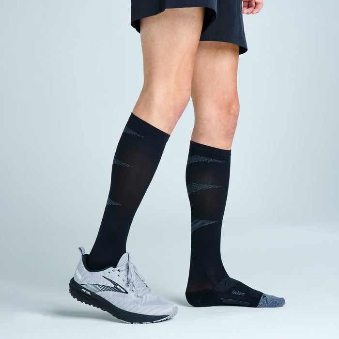 Feetures Graduated Compression Light Cushion Socks in black with gray accents, knee-high design, worn by a person standing.