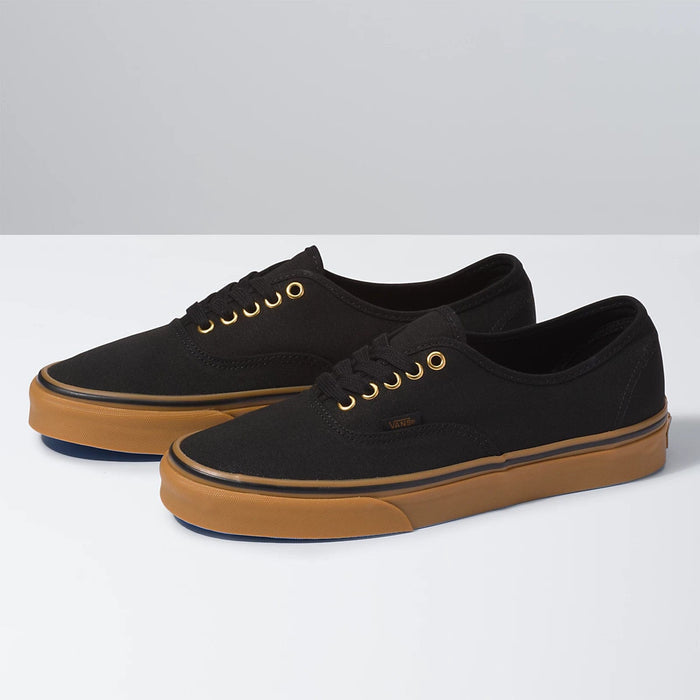 Vans Gum Authentic sneakers with black canvas upper, gum outsole, and gold eyelets, side angle view.