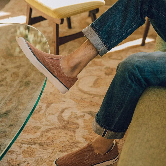 SeaVees Hawthorne Slip On shoes in textured brown canvas with white rubber sole worn by seated person indoors.