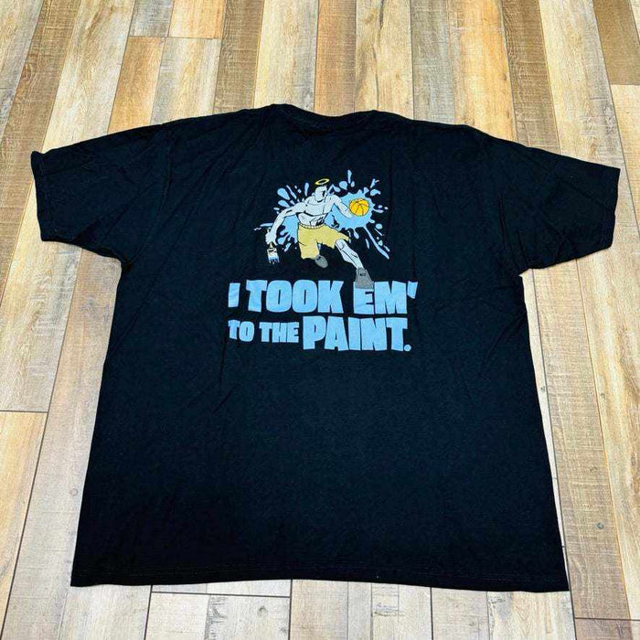 Holy Ground HG And-1 Tee in black, featuring a small white chest logo, is laid flat on a wooden floor.