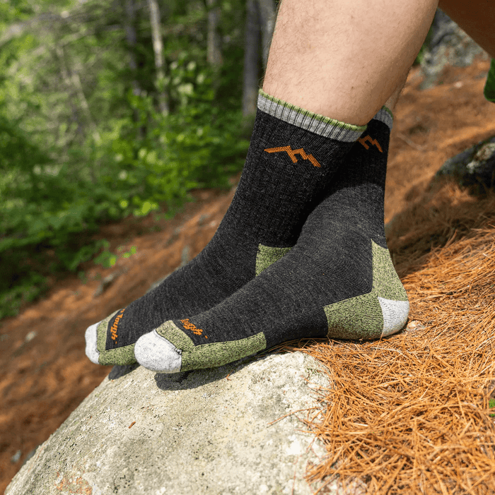 Darn Tough Hiker Micro Crew Cushion socks in charcoal gray with green and orange accents, worn outdoors on a rocky trail.