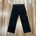 Holy Ground Cargo Black pants laid flat on wooden floor with cargo pockets and brand logo.