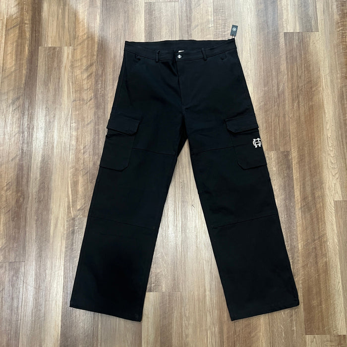 Holy Ground Cargo Black pants laid flat on wooden floor with cargo pockets and brand logo.