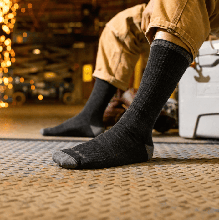 Darn Tough John Henry Boot Midweight Work Sock in black and gray with reinforced toe and heel, worn by seated worker.