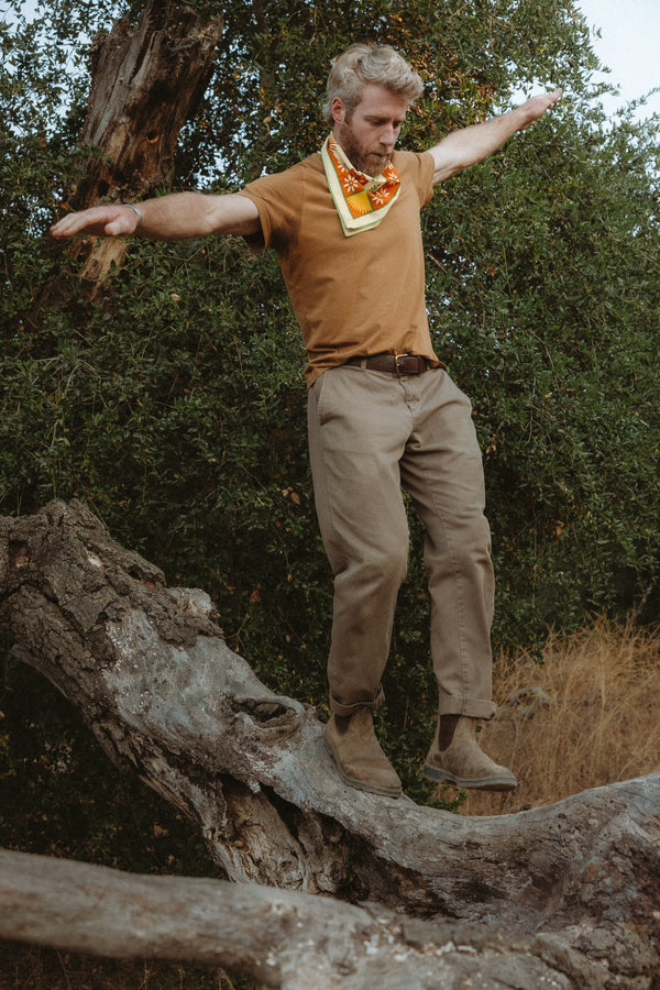 Bandits "La Magia De Tochtli" Bandana in vibrant orange and yellow with intricate nature-inspired design, worn around the neck outdoors.