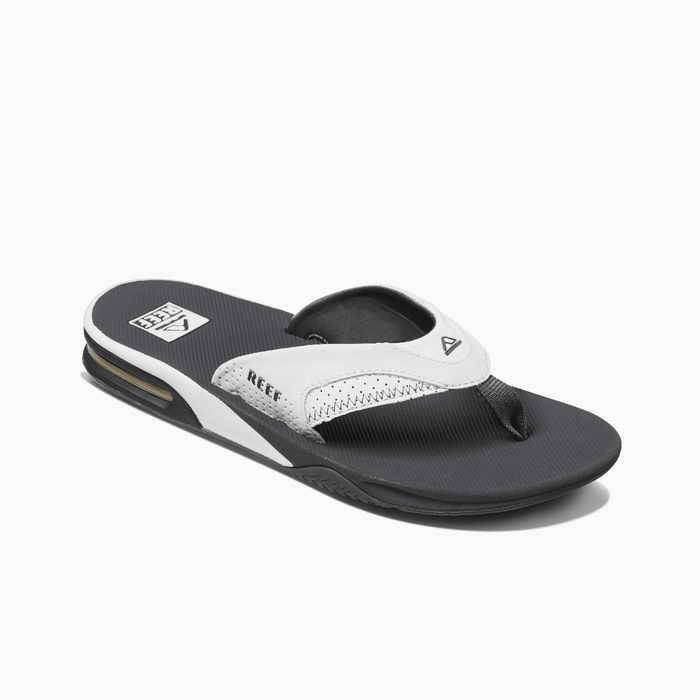 Reef Leather Fanning Flip Flops in black and white with leather straps, textured footbed, and built-in bottle opener, angled side view.