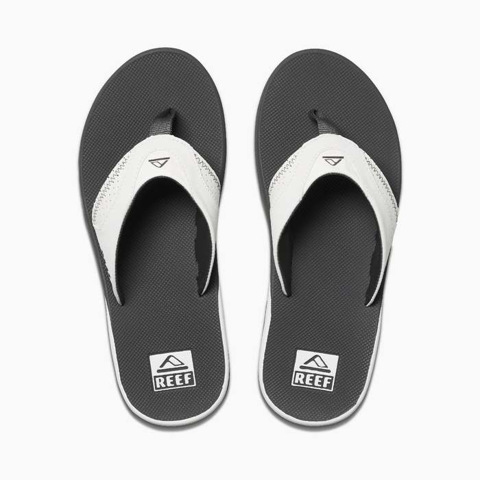 Reef Leather Fanning flip flops with black textured footbed, white leather straps, and logo detailing, top view.
