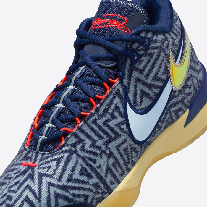 Nike LeBron NXXT Genisus basketball shoes in navy with bold zigzag patterns, red accents, and a yellow gradient Swoosh, close-up side view.