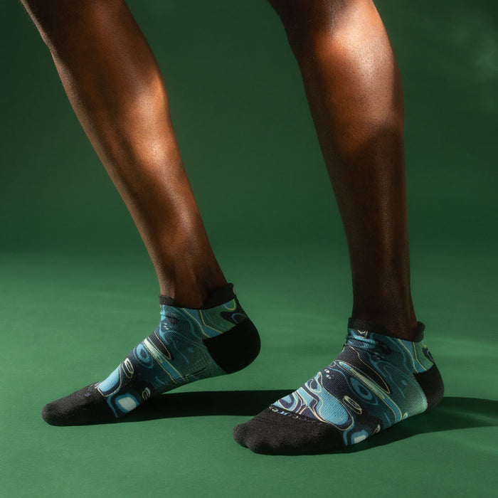 Feetures Limited Edition Elite Light Cushion No Show Tab Socks in black and teal with abstract pattern, worn during casual movement.