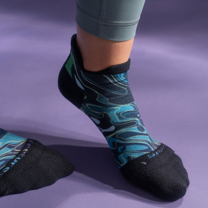 Feetures Limited Edition Elite Light Cushion No Show Tab Socks with swirling blue and green pattern, lifestyle view worn on foot.