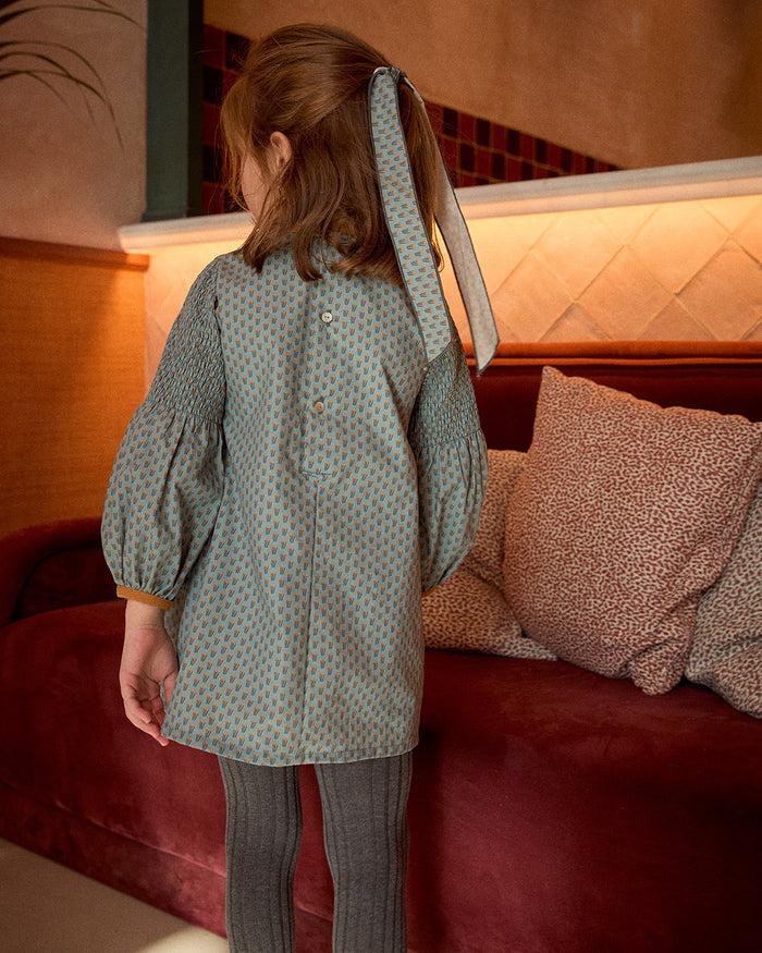 Person wearing a patterned coat standing in front of a red couch with pillows.