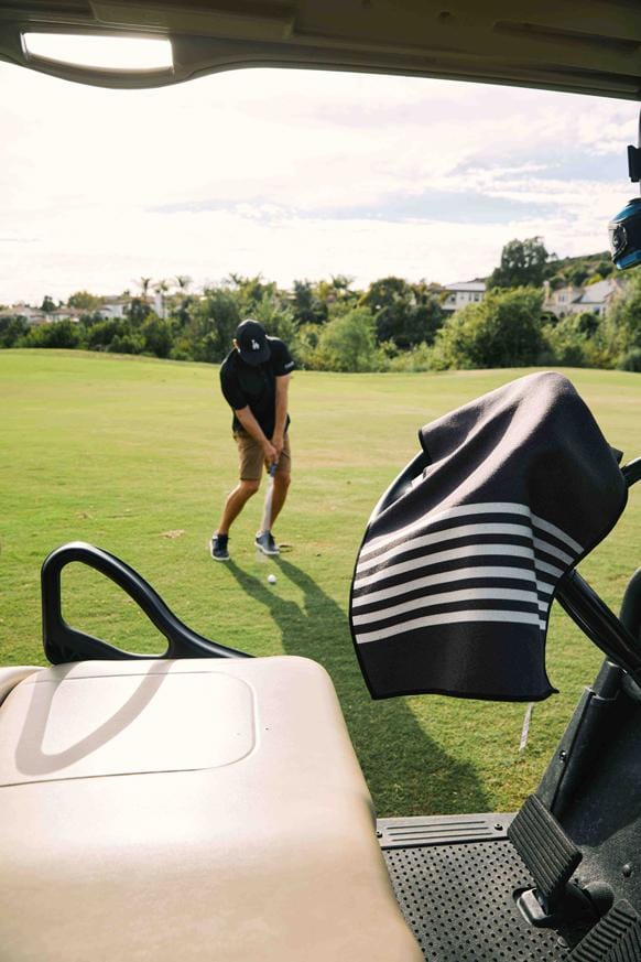 Nomadix Mini Towel in black with white striped design, hanging on a golf cart, golf course setting.