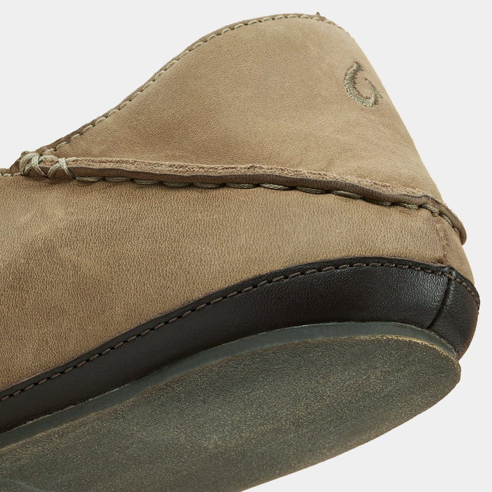 OluKai Moloa Slipper in light brown suede with stitched detailing and black leather trim, angled close-up of heel and sole.