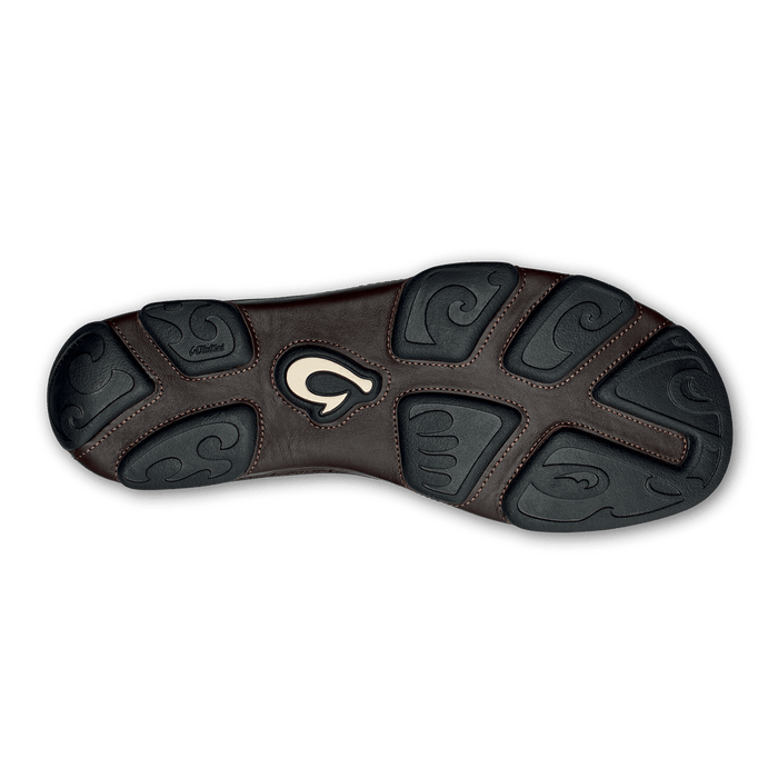 OluKai Moloa shoe outsole in dark brown leather and black rubber with intricate wave patterns and logo detail, bottom view.