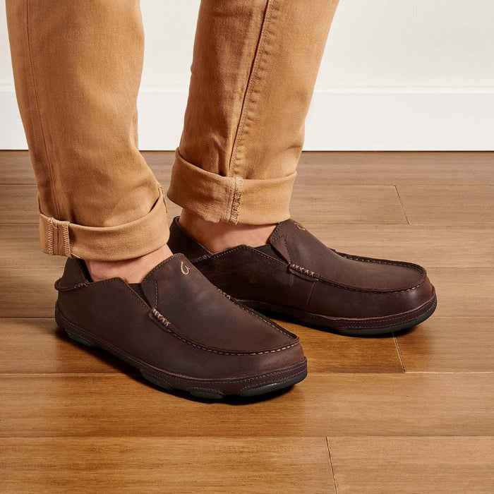 OluKai Moloa slip-on shoes in dark brown leather with moc toe stitching and foldable heel, lifestyle view.