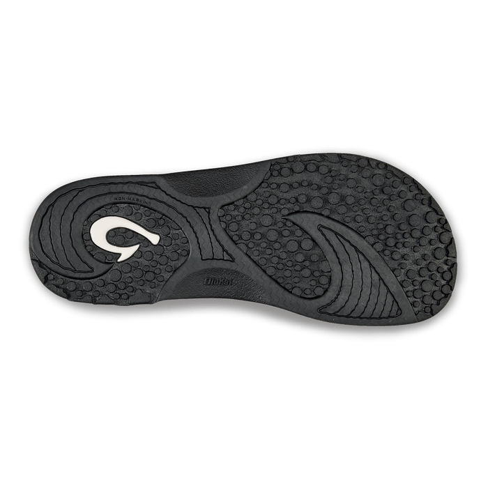 OluKai Nalu Slide sandals black rubber outsole with textured grip pattern and wave-inspired design, bottom view.