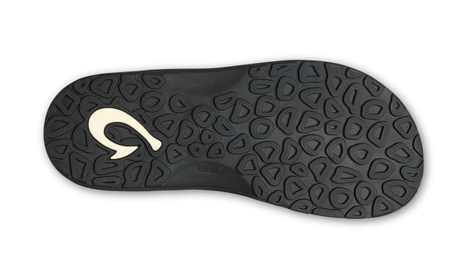 OluKai Ohana KOA sandal outsole in black rubber with textured pattern and embossed brand logo, sole/bottom view.