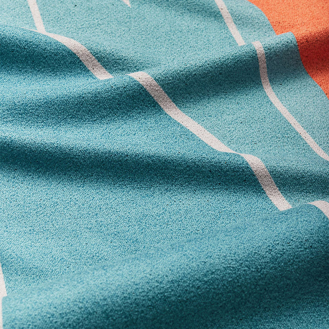 Nomadix Original Towel Big Sur featuring soft, textured material in turquoise and orange with white stripe accents, close-up view.