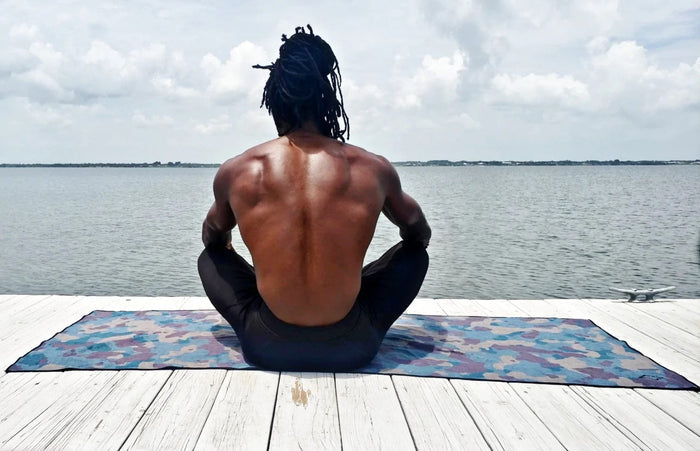 Nomadix Original Towel with colorful camo pattern, lightweight and quick-drying, used during yoga by a lake.