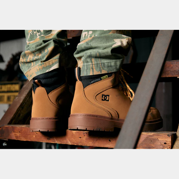 "DC WorkCrew Peary TR Work Waterproof Comp Toe Boot in tan leather with black collar and rugged outsole, lifestyle view on a wooden ladder"