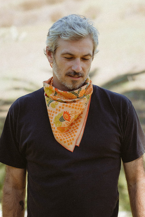 Bandits "Prickly Pollinators" bandana in vibrant orange with floral and cactus pattern, styled around the neck.