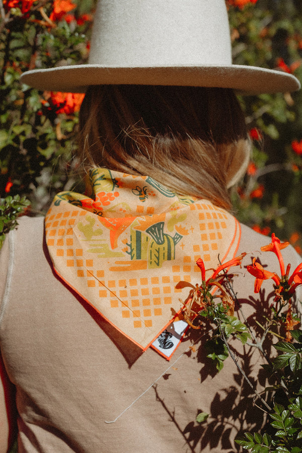 Bandits "Prickly Pollinators" bandana in orange and green with cactus and flower illustrations, worn outdoors.