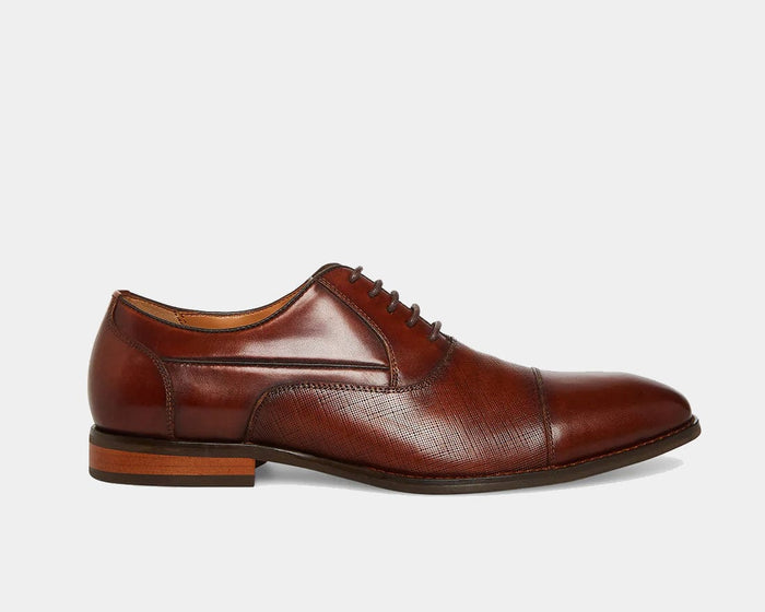 Steve Madden Proctor dress shoes in rich brown leather with textured detailing, closed lacing, and low stacked heel, side view.
