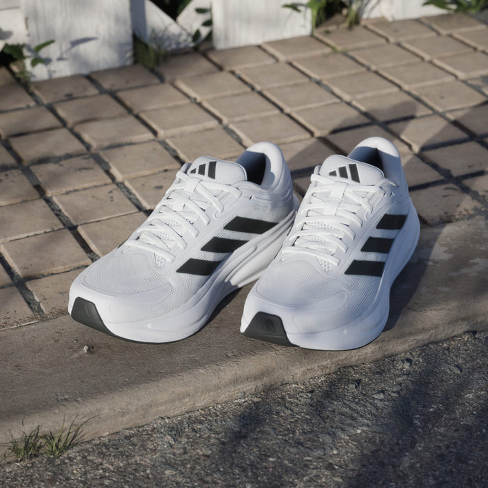 Adidas Response 2 running shoes in white with black stripes, mesh upper, and cushioned sole, outdoor lifestyle setting.