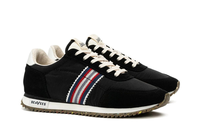 SeaVees Royal Runner sneakers in black with white soles, multicolored stripe detail, beige laces, and textured outsoles, angled side view.
