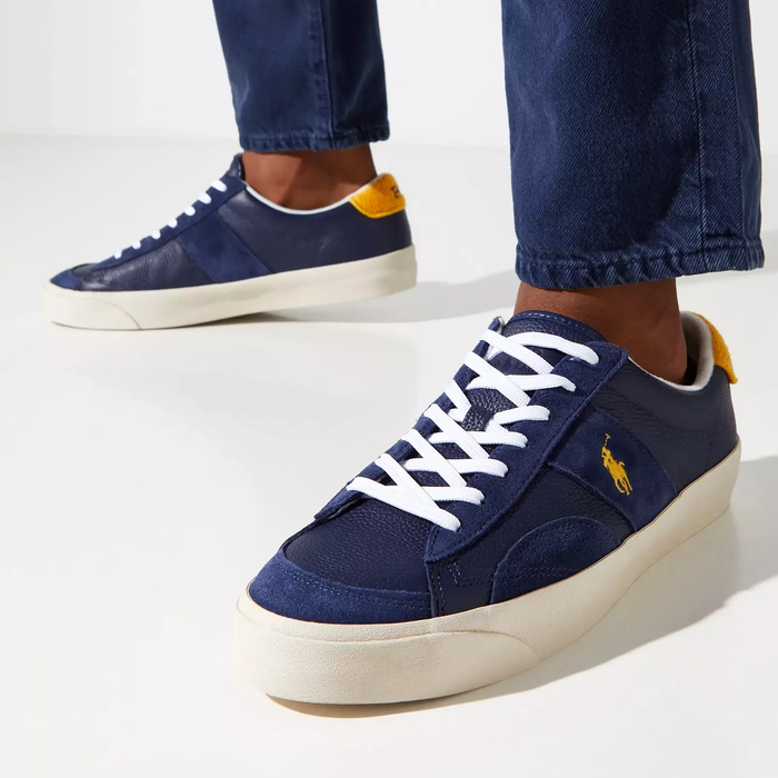 Polo Ralph Lauren Sayer Leather-Suede sneakers in navy blue with yellow logo embroidery, white laces, and off-white outsole worn casually.