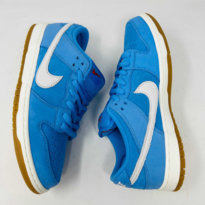 The Nike SB Dunk Low Pro University Blue Gum sneaker, featuring a white swoosh, laces, midsole, and gum-colored outsole, is placed on a brown shoebox with an orange swoosh against a plain white background.
