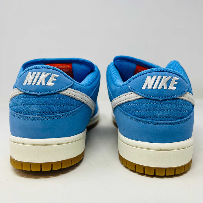 The Nike SB Dunk Low Pro University Blue Gum sneaker, featuring a white swoosh, laces, midsole, and gum-colored outsole, is placed on a brown shoebox with an orange swoosh against a plain white background.