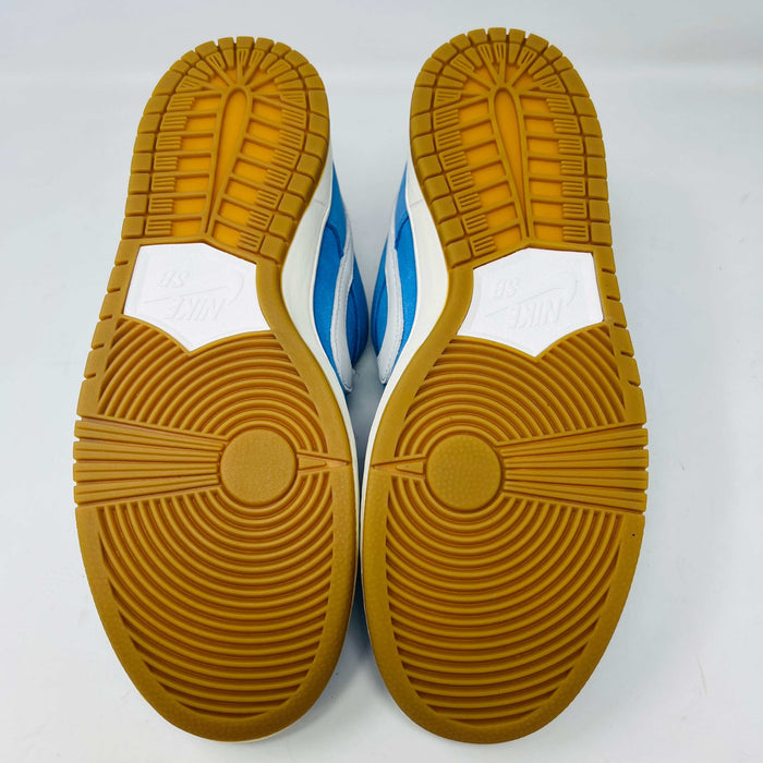The Nike SB Dunk Low Pro University Blue Gum sneaker, featuring a white swoosh, laces, midsole, and gum-colored outsole, is placed on a brown shoebox with an orange swoosh against a plain white background.