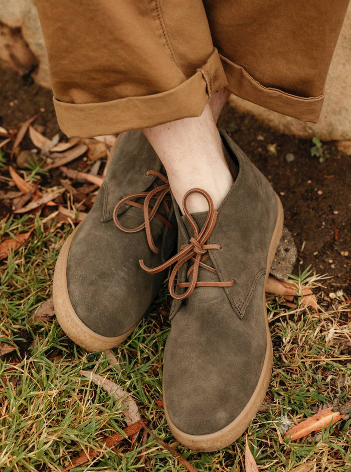 SeaVees Sun-Tans Chukka shoes in olive green suede with brown leather laces and gum soles, worn outdoors on grassy terrain.
