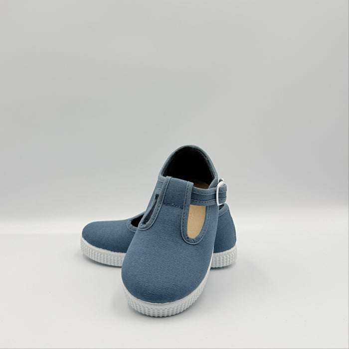 A pair of blue canvas slip-on shoes with white soles, displayed on a light gray studio background.