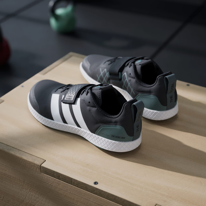 Adidas THE TOTAL 2 training shoes in black and white with green accents, durable upper, and textured midsole, side angle view on gym box.