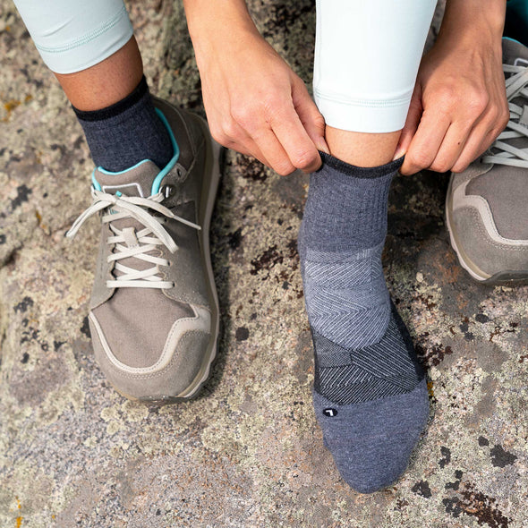 Feetures Trail Max Cushion Quarter Sock in dark gray with targeted compression and moisture-wicking fabric, worn outdoors.