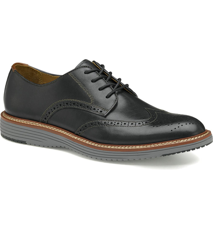 Johnston & Murphy Upton Wingtip dress shoe in black leather with brogue perforations, contrast stitching, and gray rubber sole, angled side view.