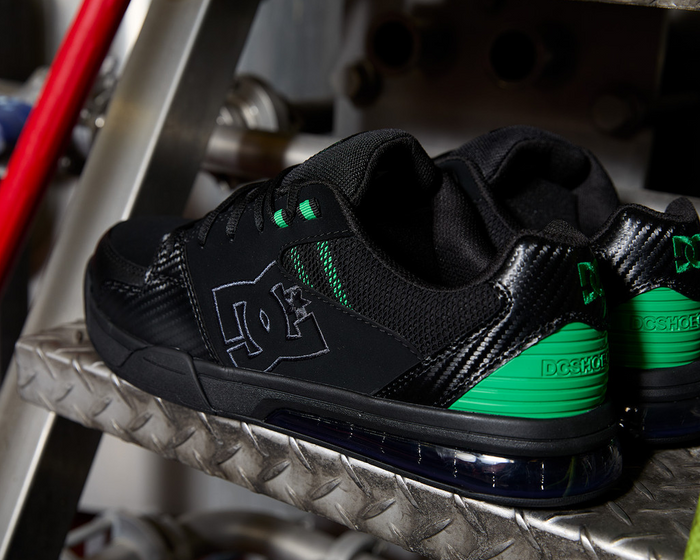 DC WorkCrew Versatile Work Comp Toe work shoes in black with green accents, composite toe protection, and durable design, side view on metal stairs.