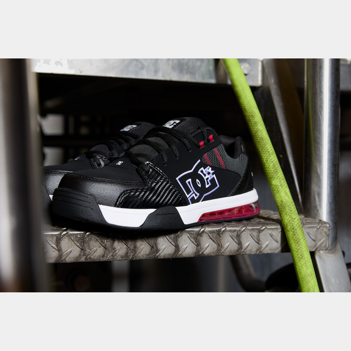 DC WorkCrew Versatile Work Comp Toe shoes in black with white DC logo, red accents, and durable comp toe, side view on industrial surface.